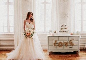 Image of bride holding a boutique of flowers standing next to a dresser with the words love on it
