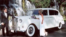 Image of bride and groom taking their wedding pictures on an antique Rolls Royce